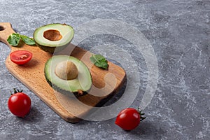 Ripe avocado cut for two parts with cherry tomato on wooden board