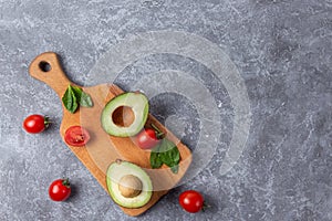 Ripe avocado cut for two parts with cherry tomato on wooden board