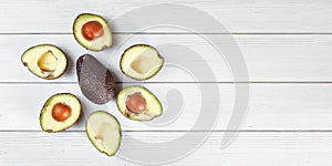 Ripe avocado halves arranged around whole dark brown pear hass / bilse fruit variety on white boards desk, banner with space for