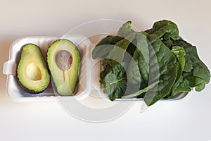 Ripe avocado and spinach leaves in white paper plates. View from above