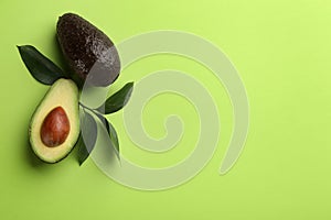 Ripe avocadoes and leaves on green background  flat lay. Space for text