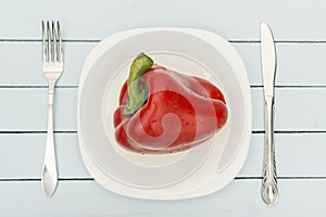 Ripe bell pepper on white plate with cutlery. Top view on wooden table. Vegetarian food concept