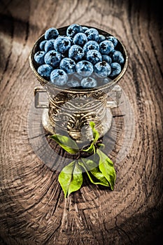 Ripe bilberries in vintage metal bowl on grunge board