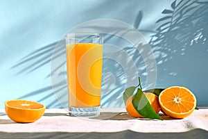 Ripe bio oranges and a glass of fresh squeezed orange juice on light blue background with leaves shadows. Organic Sicilian oranges