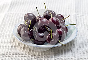 Ripe black cherries in small bowl isolated on white cloth background