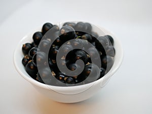 Ripe black currant berries in a small white Cup on a white background. Black currant harvest. Natural vitamin. Healthy food. veget
