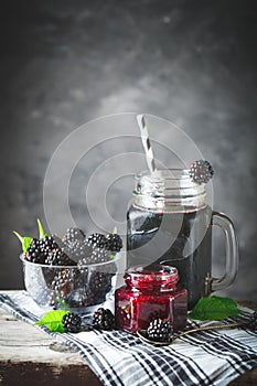 Ripe blackberry, blackberry juice and jam on a wooden table. Dark background.