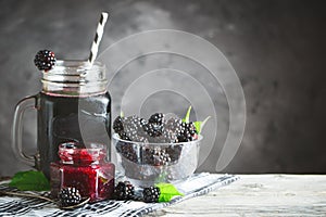 Ripe blackberry, blackberry juice and jam on a wooden table. Dark background.