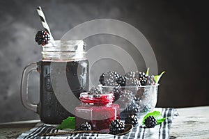 Ripe blackberry, blackberry juice and jam on a wooden table. Dark background.