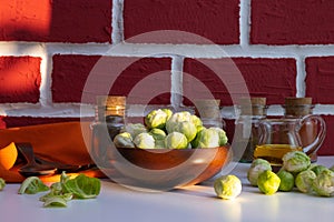 Ripe brussels sprouts in a wooden bowl stands on a white table, near spices and oil