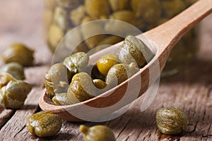 Ripe capers in a wooden spoon closeup on a background of a jar