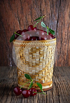 Ripe cherries in a birch bark dish on a wooden table. Green leaves. Photo