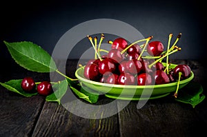 Ripe cherries with leaves in a plate on vintage table. Still life of sweet cherry after harvest