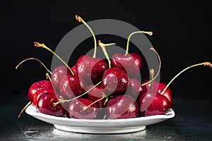 Ripe cherry berries with drops of water on a saucer on a black background