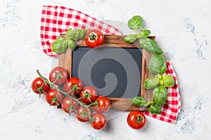 Ripe cherry tomatoes and fresh basil leaves on stone table with chalkboard, cooking ingredients top view