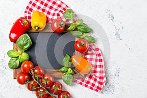 Ripe cherry tomatoes, mini bell peppers, fresh basil leaves on stone table with chalkboard, cooking ingredients, top view