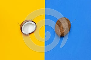 Ripe coconut on yellow and blue colored background, minimal flat lay style top view with copy space. Pop art design, creative