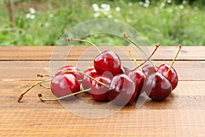 Ripe dark red cherries on a brown wooden table against green grass background