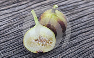 Ripe figs and halved fruit are placed on a wooden table. Pear-shaped fruit with soft, dark flesh and many small seeds, eaten fresh