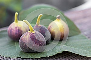 Ripe figs and leaf are placed on a wooden table. Pear-shaped fruit with soft, dark flesh and many small seeds, eaten fresh or