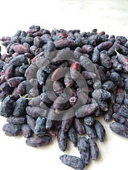 Ripe first berries of honeysuckle.  Small purple and blue berries on a white background.  A lot of fresh berries with leaves.