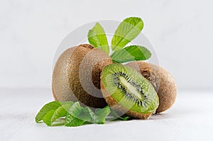 Ripe fleshy green kiwi with juicy slice, young leaves on soft light white table, closeup.