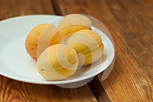 Ripe fresh apricot fruits on a white plate on the wooden background. Copy space, delisious healthy food.