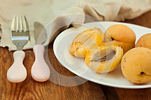 Ripe fresh apricot fruits on a white plate on the wooden background. Copy space, delisious healthy food.