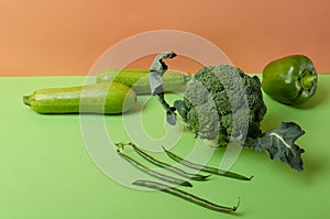 Ripe and fresh asparagus, broccoli, pepper, marrows on the green surface against orange background