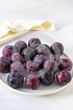 Ripe fresh damsons on a white ceramic plate. Story format