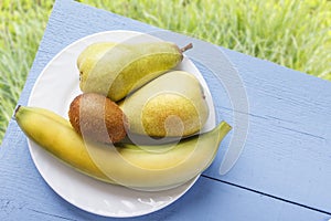 Ripe fresh fruits on wooden blue table and on natural grasses background. Banana, kiwi fruit and pear for healthy nutrition. Rusti