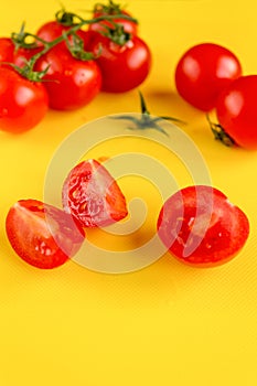 Ripe fresh Juicy organic cherry tomatoes on branch and chopped tomato on yellow plastic cutting board.  Top view