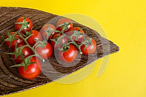 Ripe fresh Juicy organic cherry tomatoes on branch in wooden plate on yellow background