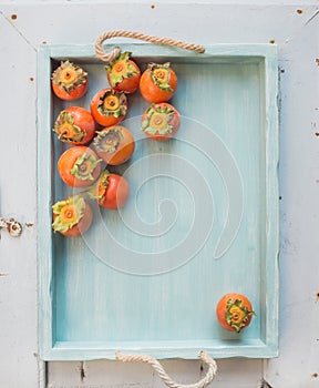 Ripe fresh persimmons on blue wooden tray over