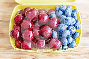 Ripe fresh tasty bio cherries and bluberries in plastic lunchbox . Organic sweet berries takeaway quick food for picnic. Healthy s