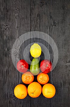 Ripe fruits and citrus fruits lie symmetrically on an old black wooden table