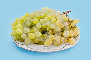 Ripe grapes in a plate on a blue background. Kish-mish grapes