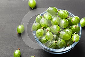 Ripe green gooseberries in a glass transparent bowl and jar on a black  background. Harvest concept agrus. Vegetarian food.Top