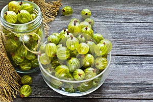 Ripe green gooseberries in a glass transparent bowl and jar on a wooden background. Harvest concept. Vegetarian food.Top view, cop