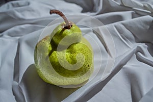 Ripe green pear on white drapery with folds in light of sun