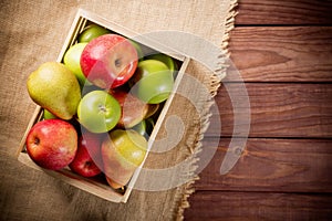 Ripe green and red apples with pears in a wooden box on sackcloth and brown wooden rustic background. Autumn seasonal image with