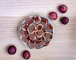 Ripe halved figs in a plate and whole figs on a wooden table close up. Ripe juicy fruits. Fresh harvest