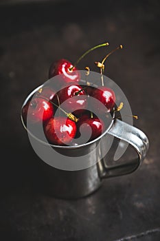 Ripe and juicy cherries in old metal cup on the dark rustic background