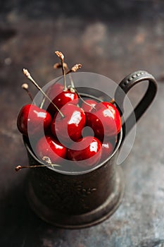 Ripe and juicy cherries in old metal cup on the dark rustic background