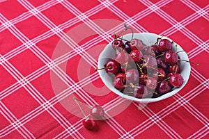 Ripe juicy cherries with water drops in a ceramic bowl on a table with a red tablecloth. Summer berries