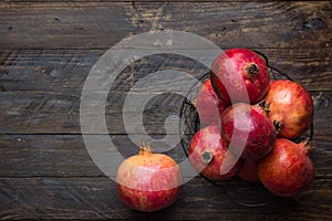 Ripe juicy organic bright red pomegranates in metal wicker basket on reclaimed plank barn wood background. Fall produce harvest