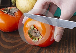 Ripe juicy persimmon cut by female hand with knife, selective focus, vegan diet