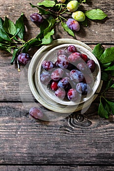 Ripe juicy plums in a bowl on a wooden background. Top view flat lay.