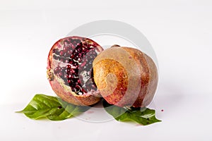 Ripe and juicy pomegranate is cut into two parts with leaves on a white background