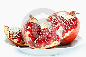 Ripe juicy pomegranate fruit (Punica granatum) in a white plate isolated on white background